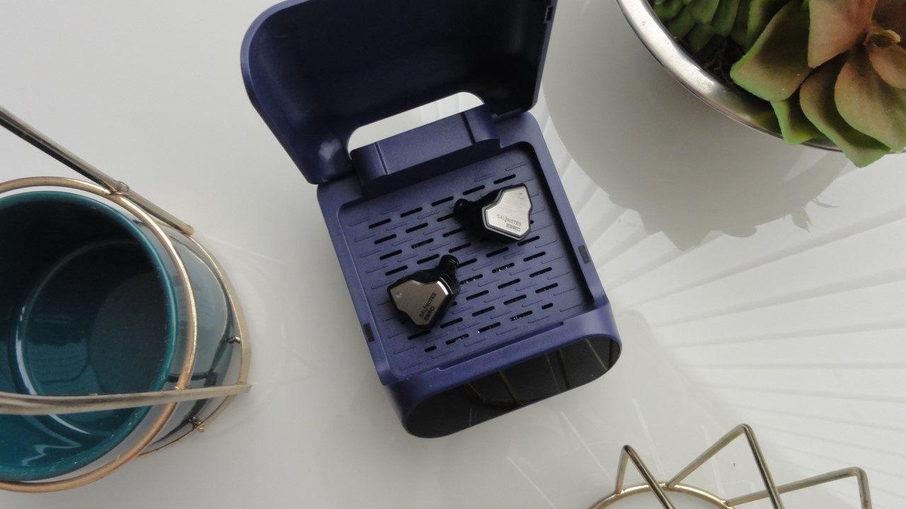 Foto do desumidificador elétrico SoundLink Aid 500 para aparelhos auditivos com bateria e fones de ouvido in-ear.