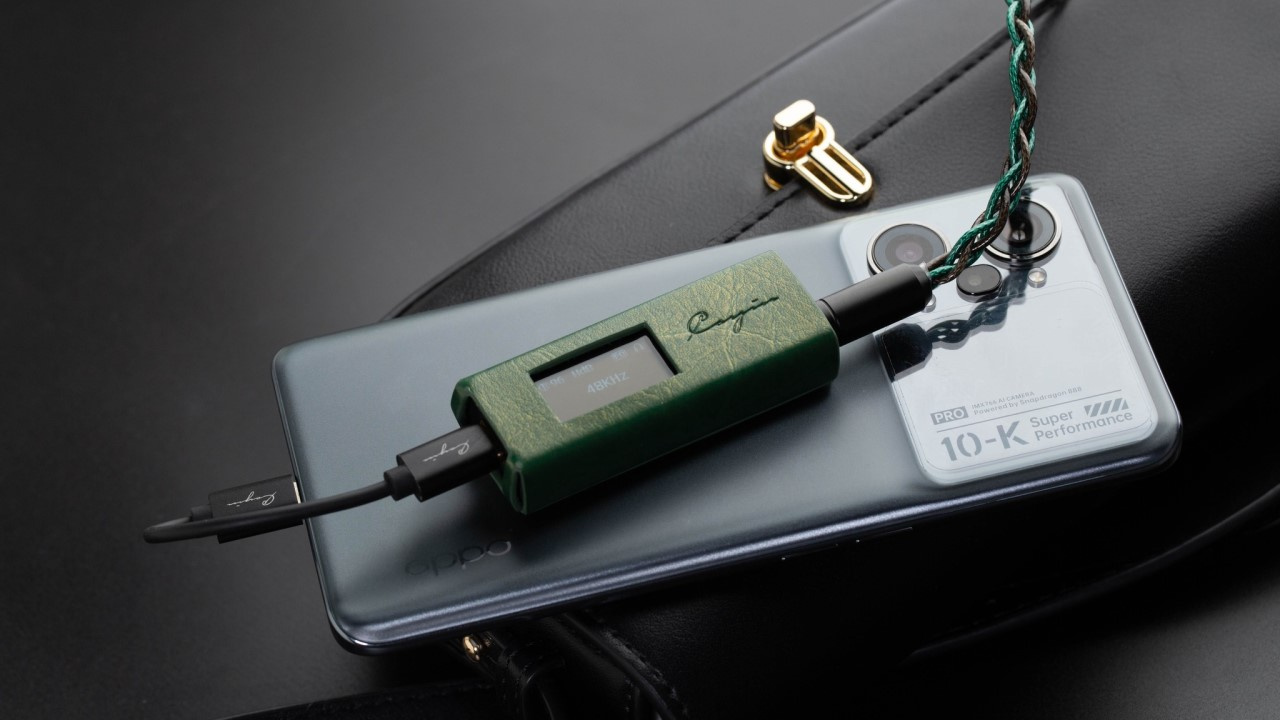 Foto do DAC/amp portátil ("dongle") Cayin RU7 conectado via USB a um celular.